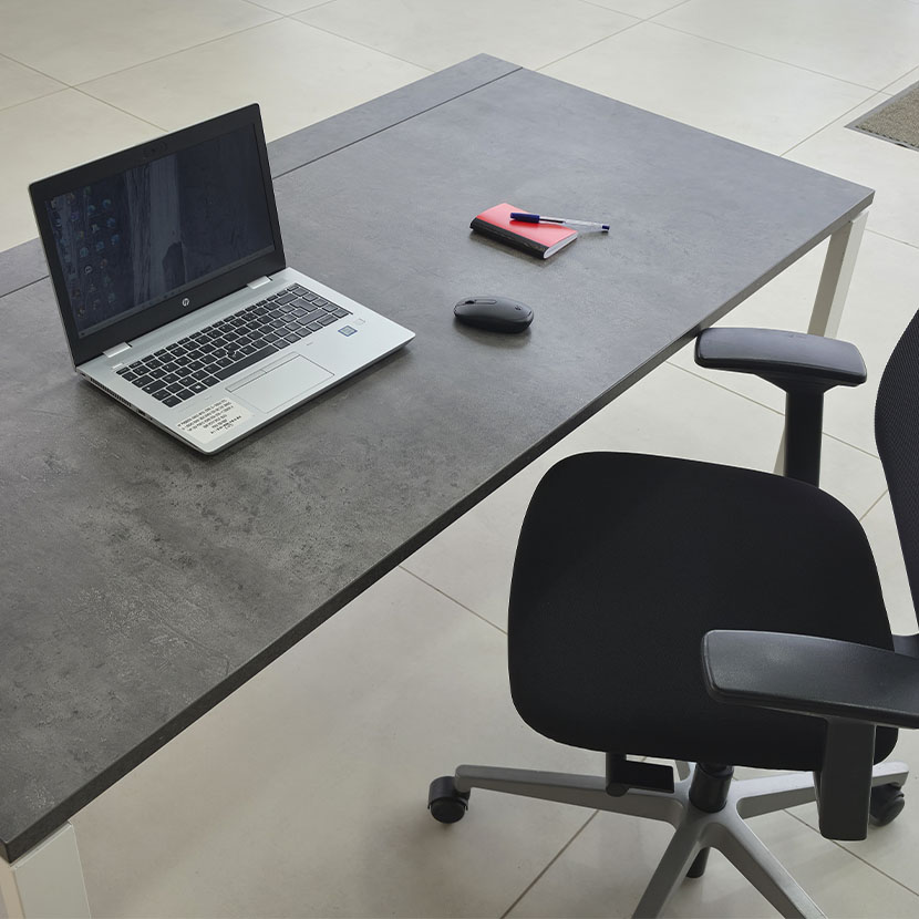Table de bureau professionnelle avec plateau gris béton, piètement métallique blanc et grande surface de travail.