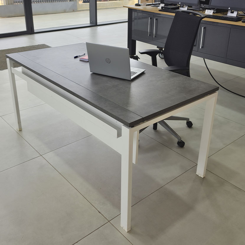 Table de bureau professionnelle avec plateau gris béton, piètement métallique blanc et grande surface de travail.