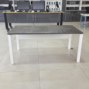 Table de bureau professionnelle avec plateau gris béton, piètement métallique blanc et grande surface de travail.
