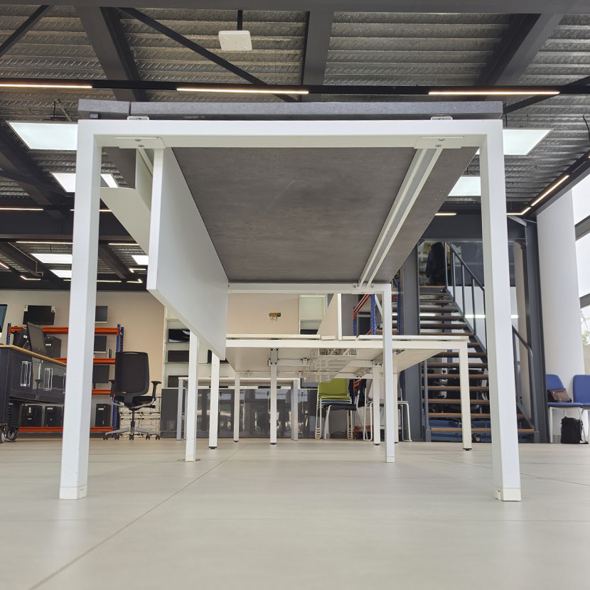Vue de dessous d'une table de bureau professionnelle avec plateau gris béton, piètement métallique blanc et voile de fond.